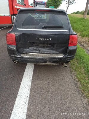 .Zdjęcie kolorowe przedstawia miejsce zdarzenia drogowego.  Na pierwszym planie zdjęcia widoczny uszkodzony pojazd marki porsche koloru czarnego. W tle widoczne są dwa pojazd uprzywilejowany Straży Pożarnej, jeden pojazd stoi przodem do Porsche drugi zaparkowany jest z lewej strony. W oddali widoczny jest znak drogowy z napisem „Żurawica”. Po lewej stonie zdjęcia widoczny jest pas zielony. Porsche zaparkowane jest na poboczu drogi