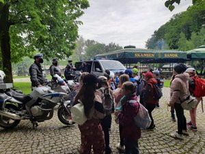 Na placu stoi policyjny radiowóz oraz dwa motocykle, umundurowani policjanci prowadza zajęcia dla dzieci.