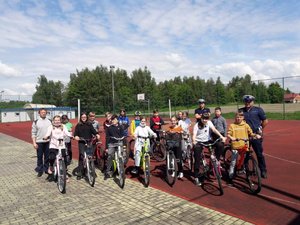 uczniowie Zespołu Szkolno – Przedszkolny w Wadowicach Górnych podczas egzaminu praktycznego na kartę rowerową, grupa młodzieży stoi na boisku sportowym na rowerach wraz z dwoma policjantami wydziału ruchu drogowego