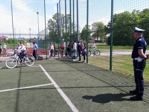 uczniowie Zespołu Szkolno – Przedszkolny w Wadowicach Górnych podczas egzaminu praktycznego na kartę rowerową, grupa młodzieży stoi na boisku szkolnym wraz z policjantem