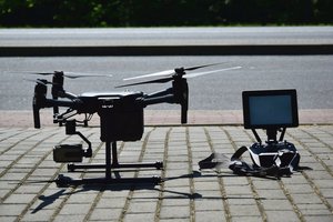 Policyjny dron stojący na chodniku. Obok, po prawej panel sterowania dronem.