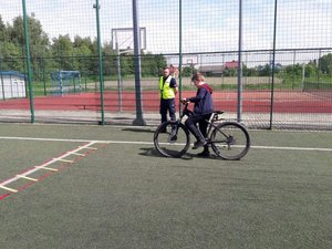 na fotografii policjant wydziału ruchu drogowego z chłopcem na rowerze na boisku szkolnym Zespołu Szkolno – Przedszkolny w Wadowicach Górnych podczas egzaminu praktycznego na kartę rowerową