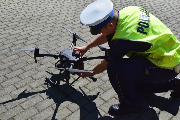Policjant ruchu drogowego w kamizelce odblaskowej obsługuje bezzałogowy statek powietrzny tzw. &quot;drona&quot;