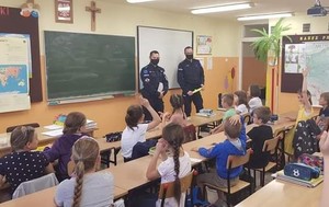 1.	Zdjęcie kolorowe przedstawia klasę szkolna . Na zdjęciu widoczni są dwaj  policjanci ubrani w granatowe mundury stoją pod ściana na której zawieszone sa trzy tablice patrząc od prawej wisi tablica multimedialna w kolorze białym następnie tablica w kolorze zielonym oraz tablica szkolna w kolorze brązowym. Przed policjantami w ławkach szkolnych siedzą dzieci z klasy III szkoły podstawowej w Stubnie. Trwają zajęcia z tematu:”  Bezpieczne wakacje”