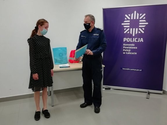 Komendant Powiatowy Policji w Łańcucie insp. Marek Mendoń podaje laureatce konkursu pamiątkowy dyplom.