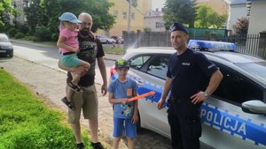 Policjant przy oznakowanym radiowozie wręcza dziecku odblask