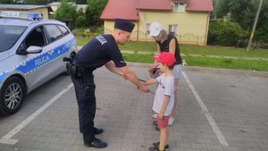 Policjant przy oznakowanym radiowozie wręcza dzieciom odblaski