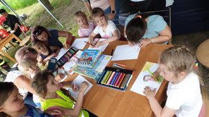dzieci siedzące przy stoliku rysujące kolorowymi kredkami na białych kartkach, dzieci biorą udział w konkursie &quot;bezpieczne wakacje&quot; zorganizowanym przez policjantki