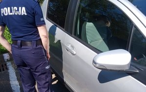 Na zdjęciu umundurowany policjant stoi przed zaparkowanym pojazdem