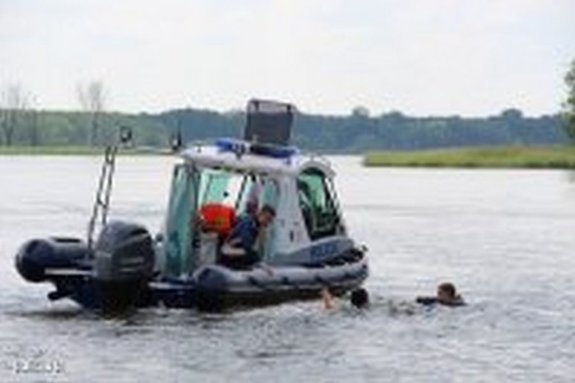 Jezioro na którym znajduje się policyjny ponton. Funkcjonariusz próbuje wyciągnąć z wody dwie osoby