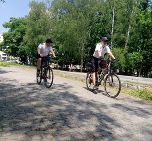 Dwóch policjantów na rowerach służbowych patrolujących rejon parku miejskiego