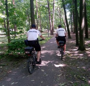 Dwóch policjantów na rowerach służbowych patrolujących rejon parku miejskiego