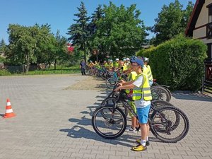 Na zdjęciu policjant ruchu drogowego w towarzystwie uczniów zdających egzamin na kartę rowerową. Dzieci stoją obok swoich rowerów.