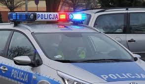 Zdjęcie kolorowe przedstawia policyjny radiowóz oznakowany z włączonymi światłami w kolorze czerwono –niebieskimi które sa umieszczone na belce.