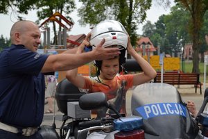 na zdjęciu policjant zakłada kask dziecku siedzącemu na motocyklu policyjnym