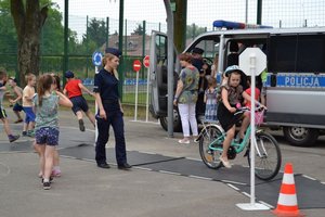 na zdjęciu policjantka przeprowadzająca dziecko na miasteczku rowerowym, w tle radiowozy i inne dzieci