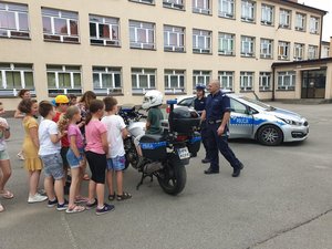 policjanci wydziału ruchu drogowego z dziećmi, w tle motocykl i radiowóz