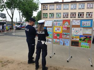 policjanci oglądający prace plastyczne dzieci, w tle inne dzieci i radiowozy
