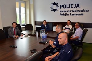Uczestnicy szkolenia siedzą w sali sztabowej przy stole. Na pierwszym planie po prawej dwaj umundurowani policjanci, dalej pozostałe osoby. W tle na ścianie napis POLICJA Komenda Wojewódzka Policji w Rzeszowie
