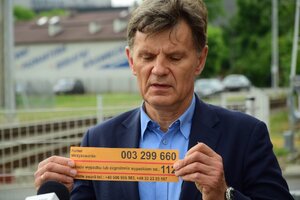 Mężczyzna w garniturze planie pokazuje żółtą naklejkę.