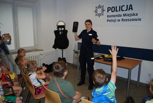 W sali w budynku w komendzie prowadząca prelekcję policjantka uczy dzieci znaków drogowych.