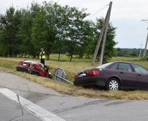 Audi i renault, uczestniczący w zdarzeniu drogowym. Oba pojazdy znajdują się w rowie. W tle widoczny policjant, pracujący na miejscu wypadku.