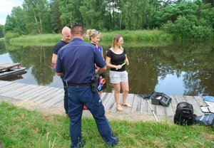 Policjant wręcza ulotki informacyjne osobom przebywającym nad zalewem wodnym w miejscowości Kamionka