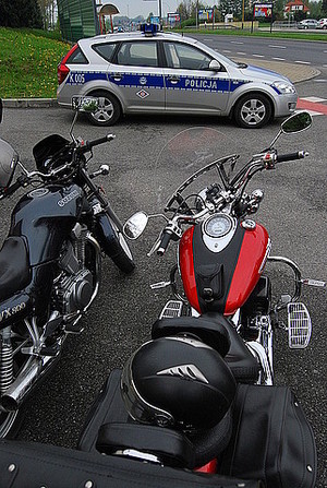 Na pierwszym planie stoją dwa zaparkowane motocykle, w tle widać policyjny radiowóz