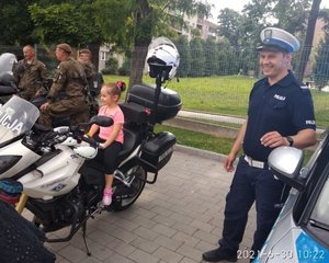 Motocykl policyjny na którym siedzi dziecko. Obok stoi policjant