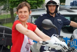 Kobieta siedzi na motocyklu policyjnym. Obok niej stoi policjant.