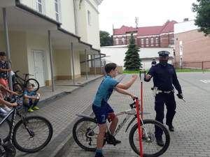 uczniowie podczas egzaminu na kartę rowerową, w tle policjant