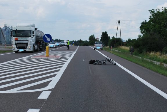 Zdjęcie kolorowe przedstawia miejscowość Zadąbrowie miejsce zdarzenia drogowego .Z lewej strony na pierwszym planie widoczna jest droga krajowa K-77 na której leży rower a przed nim zaparkowany pojazd m-ki suzuki w kolorze srebrnym. Po prawej stonie na drugiej części jezdni widoczne sa pojazdy oraz policjant w kamizelce odblaskowej kierujący ruchem.