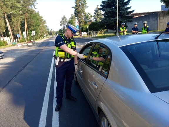 Na zdjęciu znajduje się umundurowany policjant dokonujący kontroli stanu trzeźwości osoby będącej w unieruchomionym pojeździe osobowym