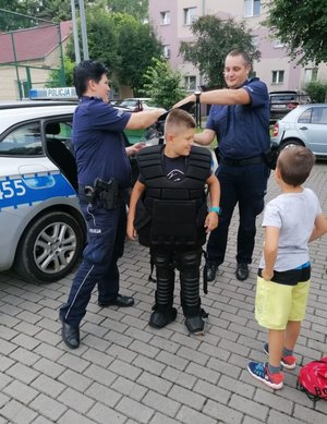 Policjanci zakładają chłopcu policyjny sprzęt.