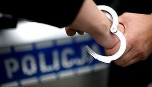 policjant zakłada kajdanki na przedramię w tle policyjny radiowóz