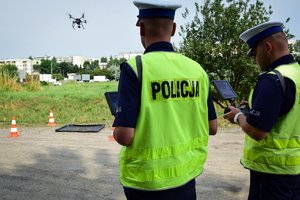 Policjanci - operatorzy drona podczas pracy. Funkcjonariusze widoczni od tyłu.