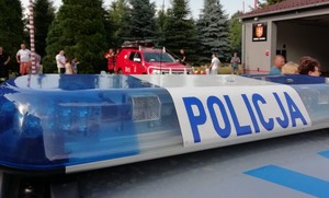 belka dachowa radiowozu z napisem &quot;policja&quot;, w tle samochód strażacki oraz mieszkańcy Krosna