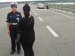 Policjantka ruchu drogowego udzielająca wypowiedzi dziennikarce. W tle policjanci prowadzący działania.