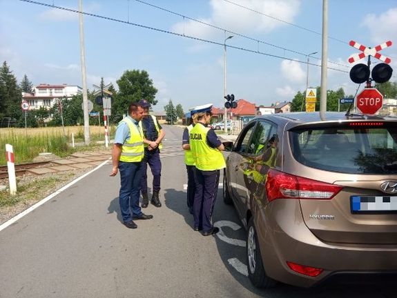 Na zdjęciu znajduje się dwóch pracowników Polskich Linii kolejowych, dwie policjantki i pojazd osobowy stojący przed przejazdem kolejowym