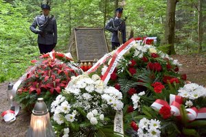 Przy obelisku upamiętniającym katastrofę śmigłowca w Cisnej stoi dwóch policjantów z kompanii honorowej. Na pierwszym planie wieńce kwiatów i znicz