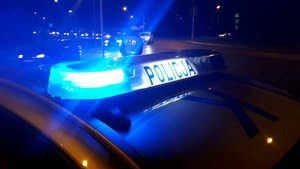 Belka policyjnego radiowozu z napisem policja. Pora nocna i świecące się sygnały błyskowe