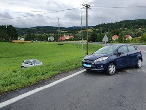 33. Zdjęcie kolorowe przedstawia miejsce zdarzenia drogowego w miejscowości Olszany. Na pierwszym planie widoczny pojazd ford koloru granatowego a po lewej stronie zdjęcia widoczny pojazd Fiat koloru srebrnego , który w wyniku uderzenia został zepchnięty z drogi na łakę.