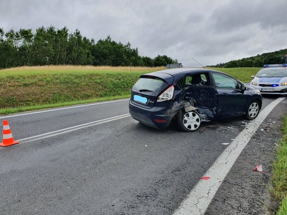 . Zdjęcie kolorowe przedstawia miejsce zdarzenia drogowego w miejscowości Olszany. Na zdjęciu widoczny pojazd ford stojący tyłem koloru granatowego , uszkodzony ma prawy pok pojazdu na wprost niego widoczny radiowóz.