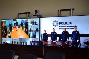 na monitorach widać uczestników wideokonferencji, po lewej ujęcia z innych komend wojewódzkich, gdzie stoja funkcjonariusze policji, na monitorze po prawej stronie przy stole stoją funkcjonariusze policji, od lewej komisarz Magdalena Kruczek naczelnik Laboratorium Kryminalistycznego, biegły, który złożył ślubowanie, inspektor Piotr Zalewski zastępca Komendanta Wojewódzkiego Policji w Rzeszowie oraz funkcjonariusz laboratorium kryminalistycznego. W tle na ścianie logo Policja i napis Komenda Wojewódzka Policji w Rzeszowie