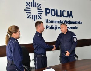 Inspektor Piotr Zalewski zastępca Komendanta Wojewódzkiego Policji w Rzeszowie gratuluje biegłemu Laboratorium Kryminalistycznego, z lewej strony komisarz Magdalena Kruczek naczelnik Laboratorium Kryminalistycznego. W tle na ścianie logo Policja i napis Komenda Wojewódzka Policji w Rzeszowie