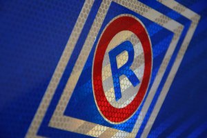 na niebieskim tle logo policji ruchu drogowego. Litera R wpisana w okrąg