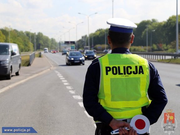 policjant ruchu drogowego trzymający w rękach skrzyżowanych z tyłu tarczę do zatrzymywania pojazdów