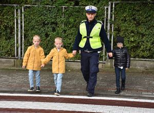 Policjant przeprowadza trójkę dzieci przez przejście dla pieszych.