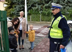 Policjant przy radiowozie. Obok niego stoją dwie kobiety z dziećmi.