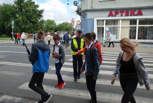 Zdjęcie kolorowe z akcji Bezpieczna droga do szkoły. Na przejściu dla pieszych widoczna jest młodzież oraz policjant ruchu drogowego. Zdjęcie zrobione w Przemyślu na ul. Jagielońskiej